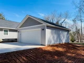 Gray detached garage with white garage door, concrete driveway, and blue sky.