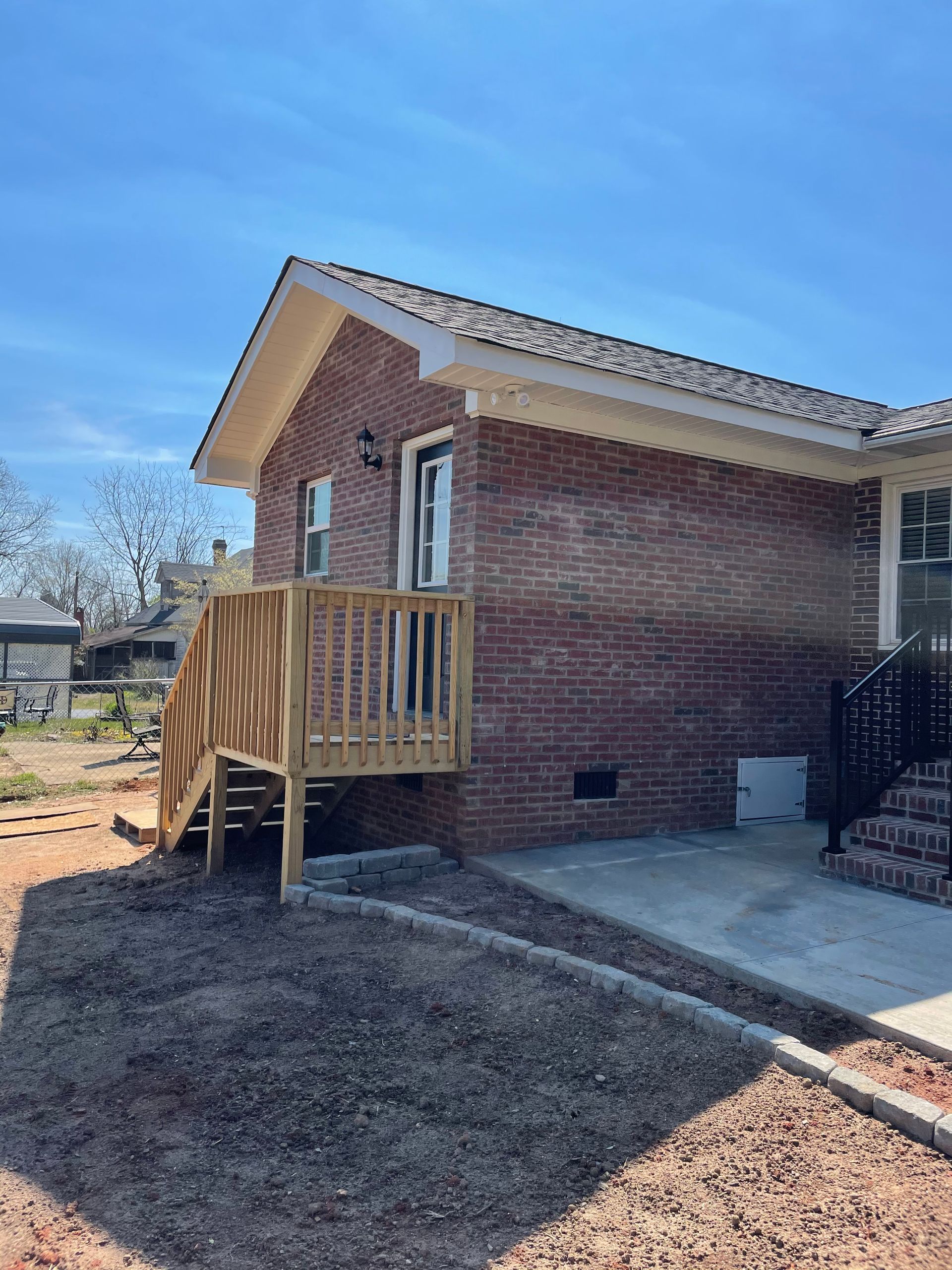 Brick house with wooden deck and ramp; gravel yard, blue sky.