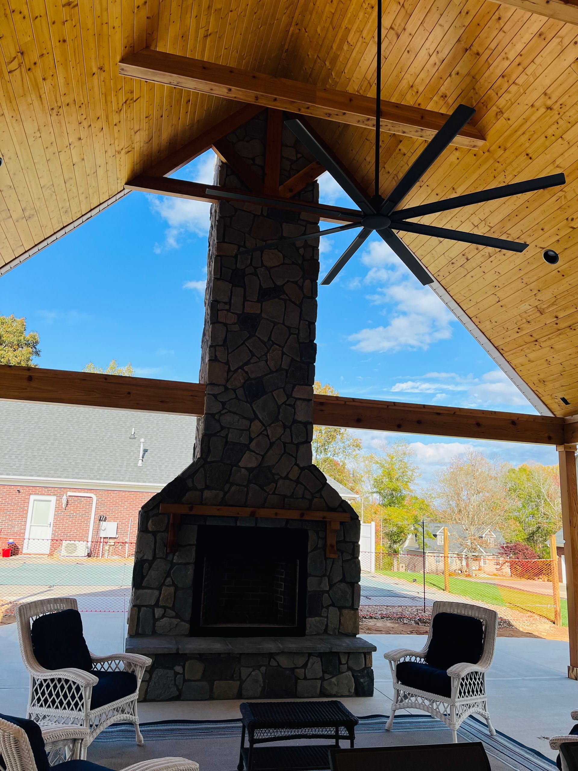 Outdoor stone fireplace with seating, under a wood-paneled ceiling, against a blue sky.