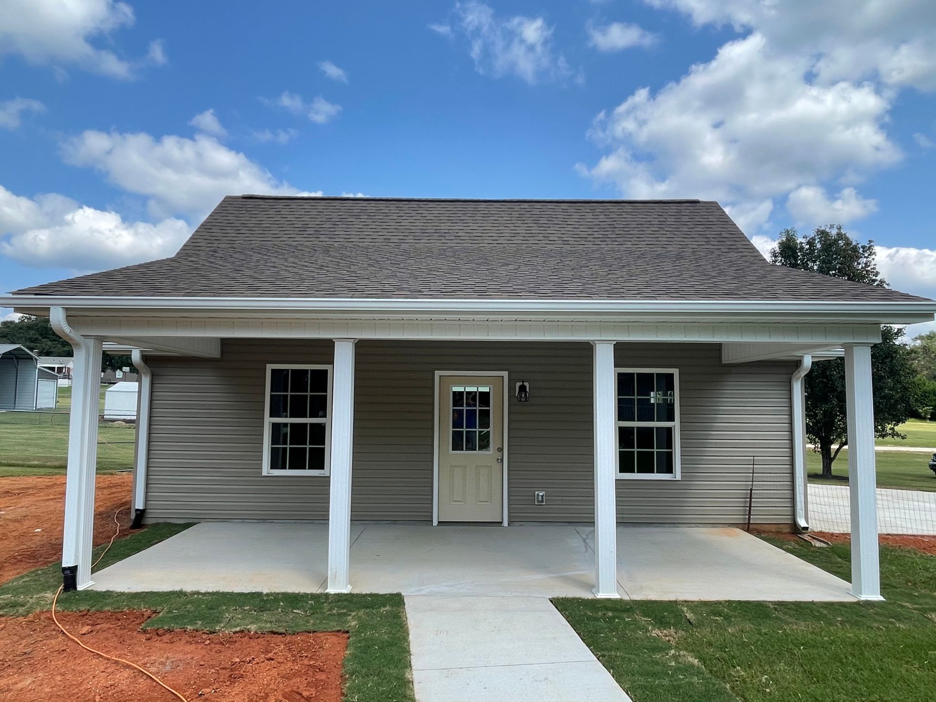Small, beige house with a porch and white pillars under a blue sky.