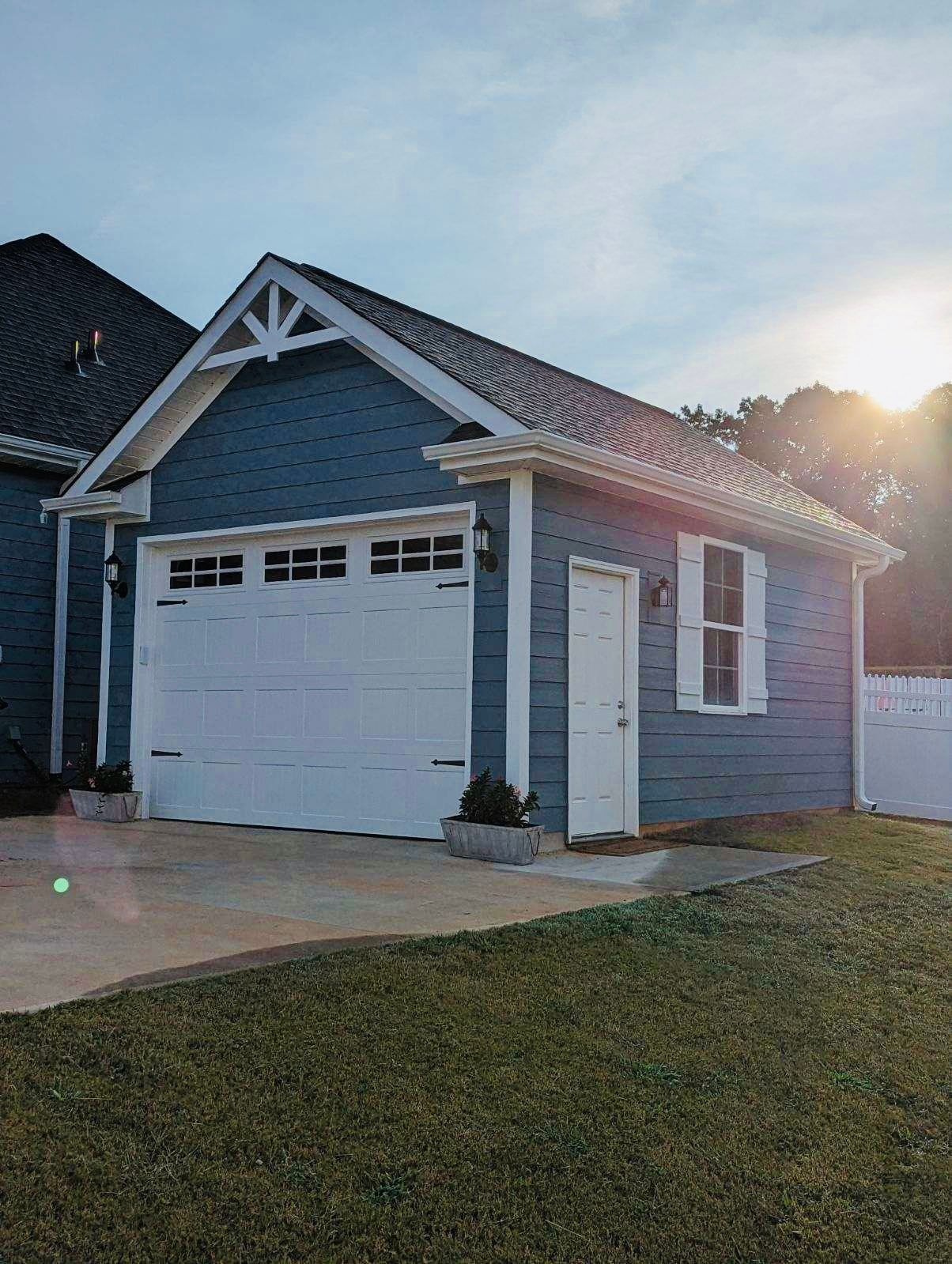 Blue garage with white trim and garage door; small door and window.