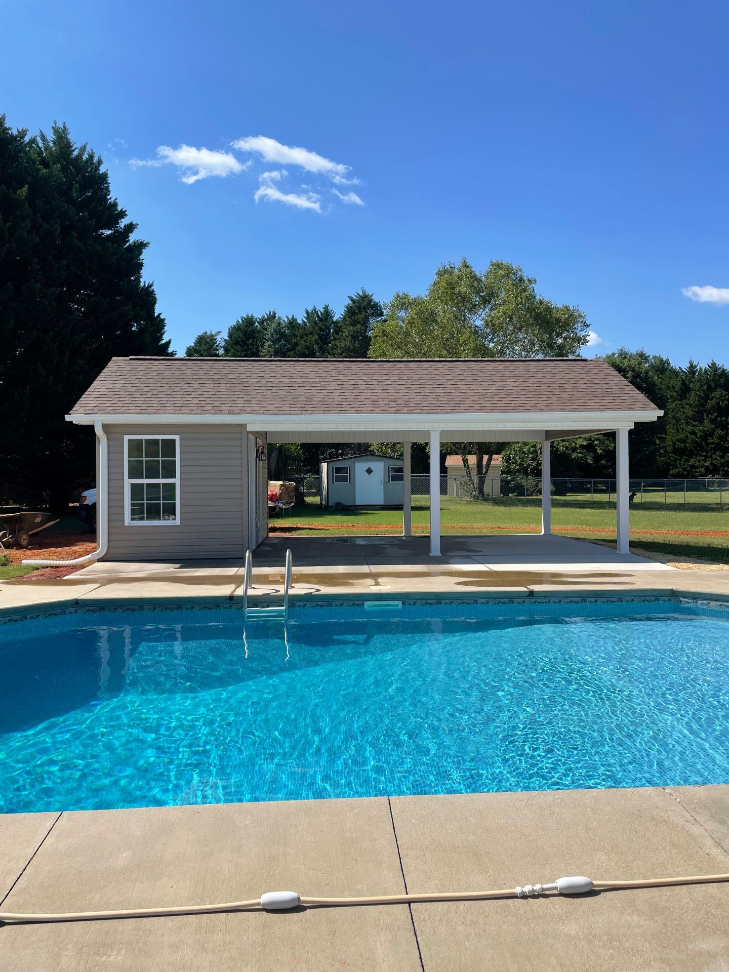 Poolside structure with pool, building with window, and covered patio under blue sky.
