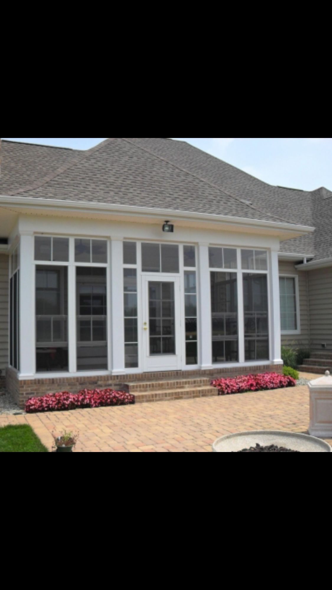 Screened porch with white frames, brick steps, and pink flowers in front of a home with a yellow roof.