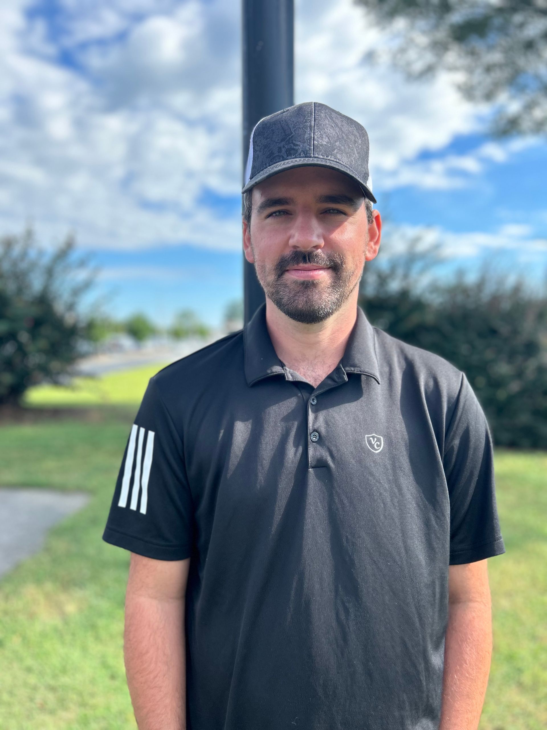 A man wearing a hat and a black polo shirt is standing in a field.