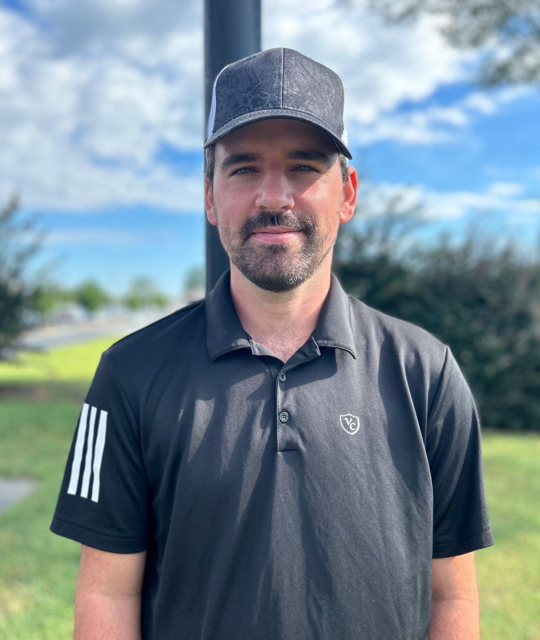 A man wearing a hat and a black polo shirt is standing in a field.
