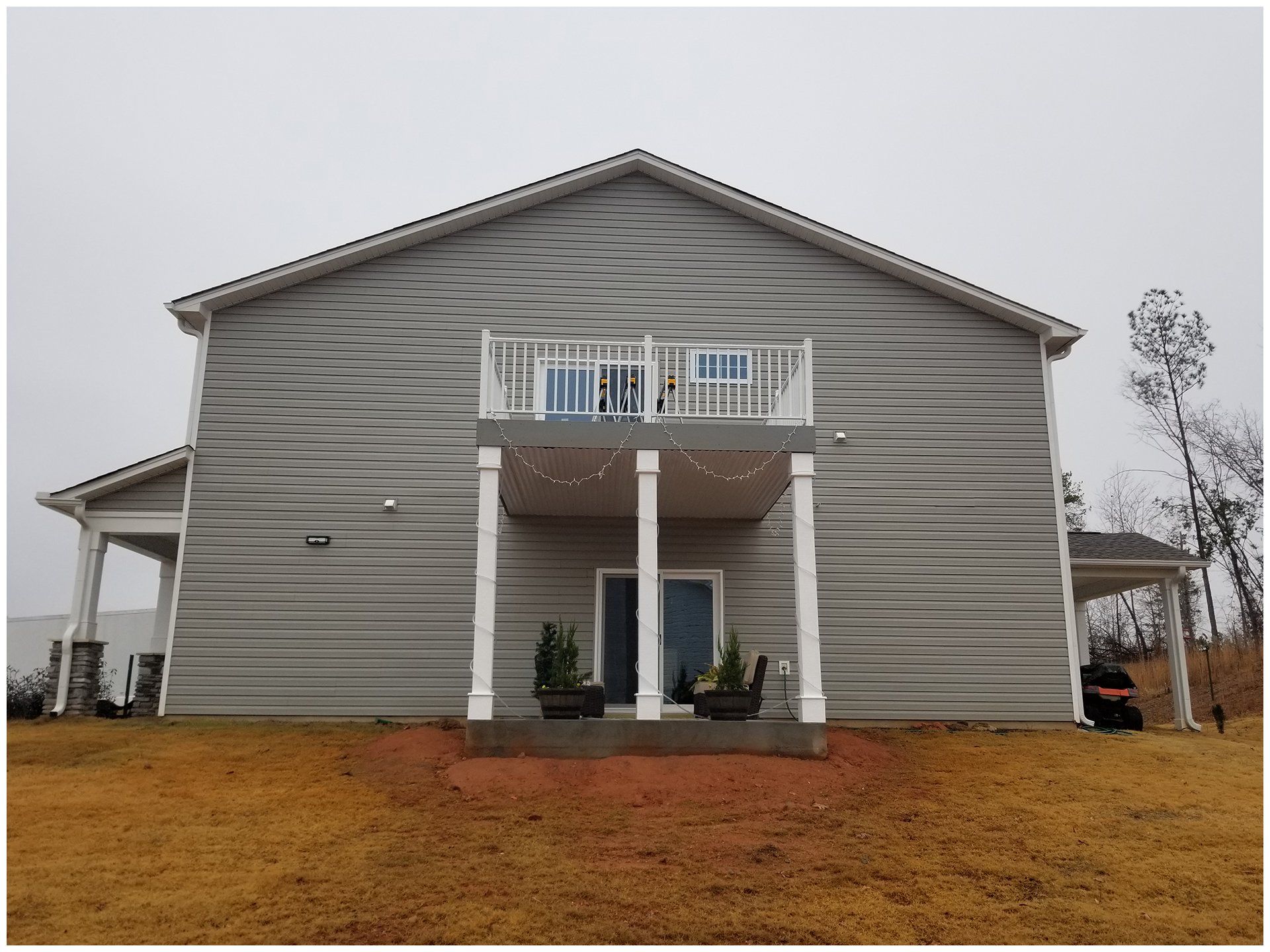 Gray house with a second-story balcony supported by white pillars. Backyard with brown grass.