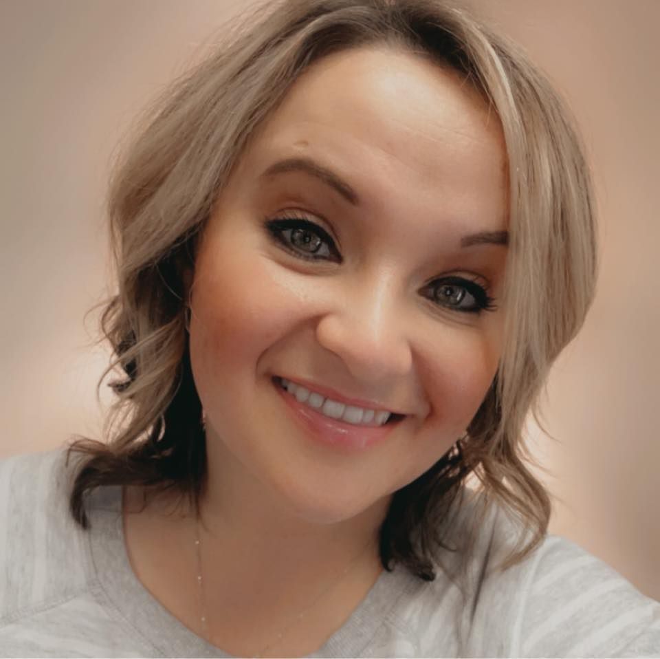 A woman is smiling for the camera and wearing a gray shirt.