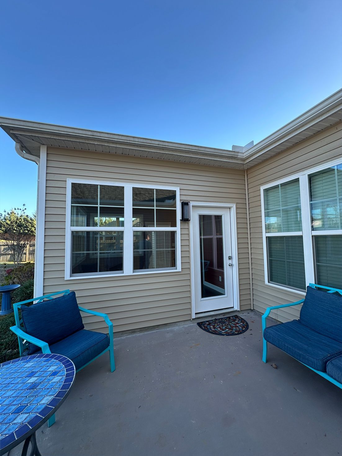 A patio with two blue chairs and a table in front of a house.