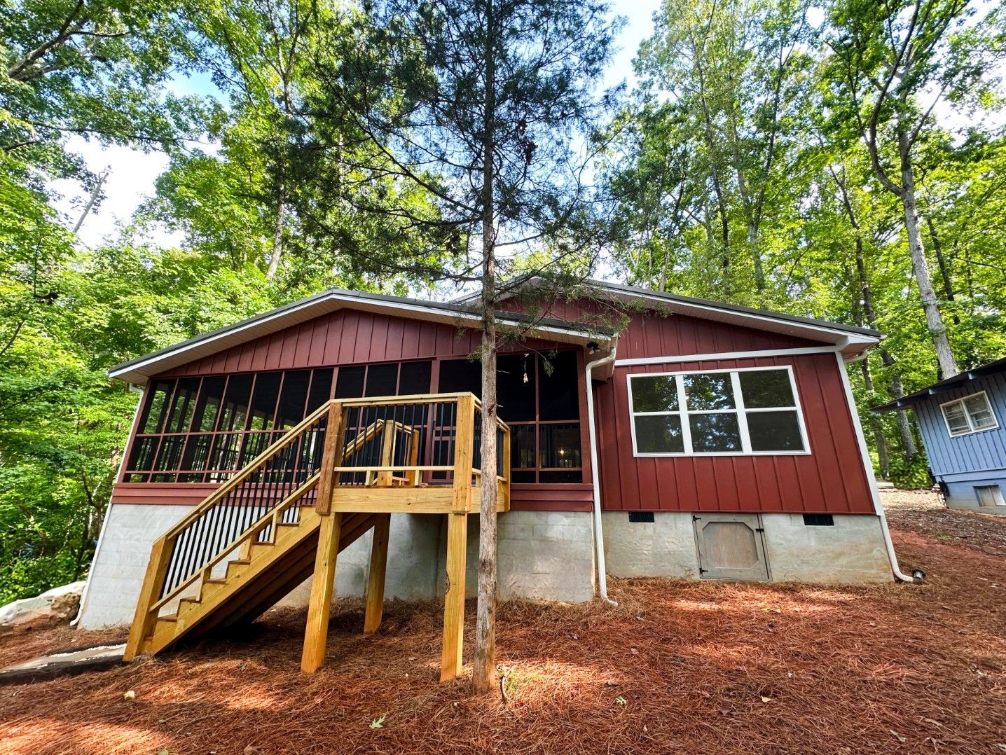 Red cabin with screened porch and wooden stairs in a wooded setting.