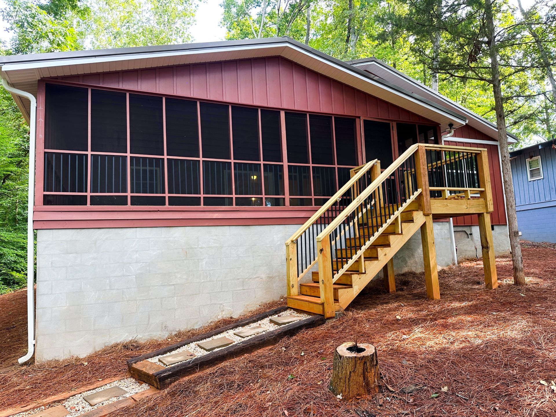 Cottage with a red exterior, screened porch, wooden stairs, and a concrete foundation.