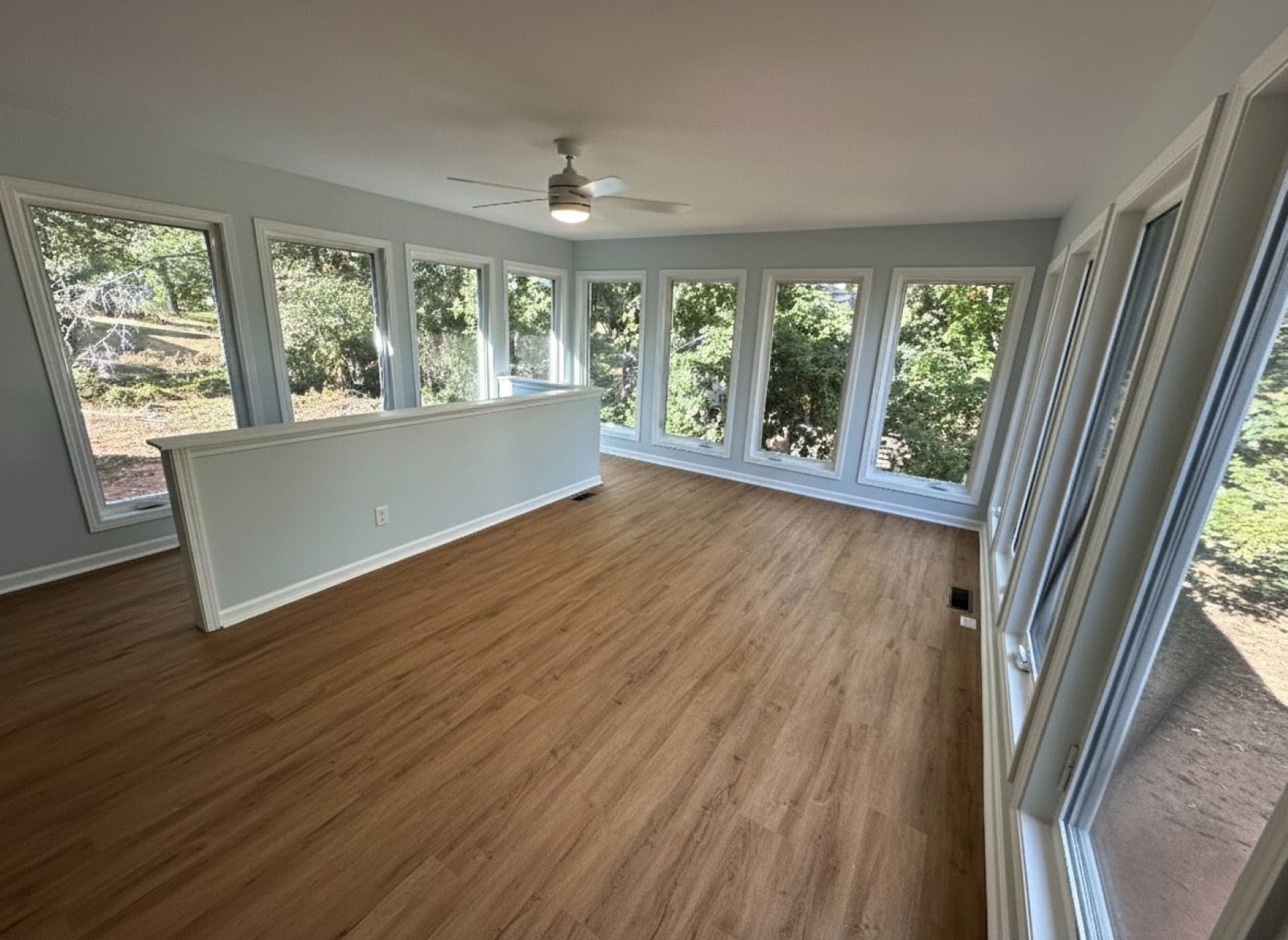 Sunroom with light blue walls, many windows, and wood-look flooring. A low wall is present.