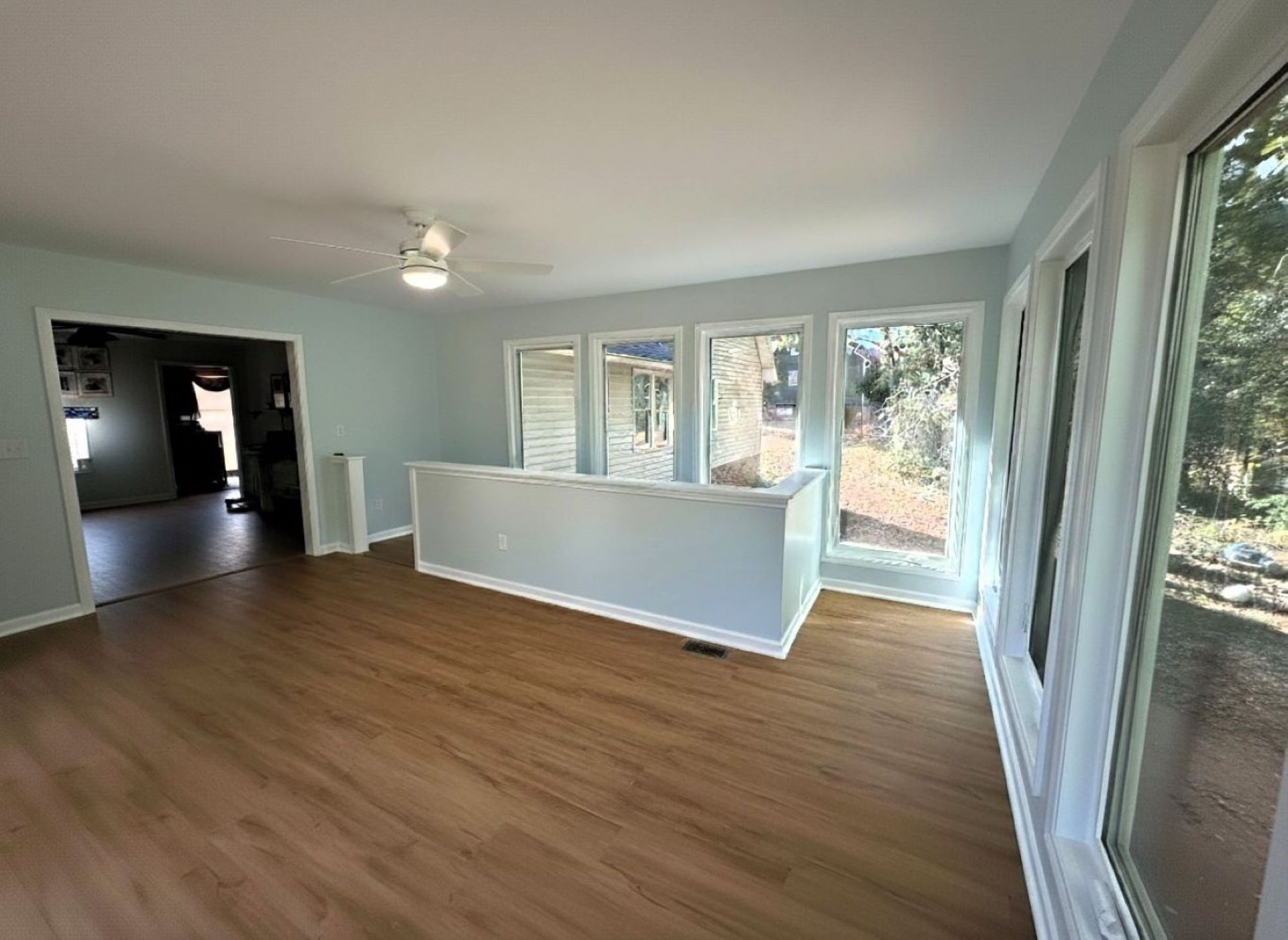 Empty room with light blue walls, large windows, and wood-look flooring.