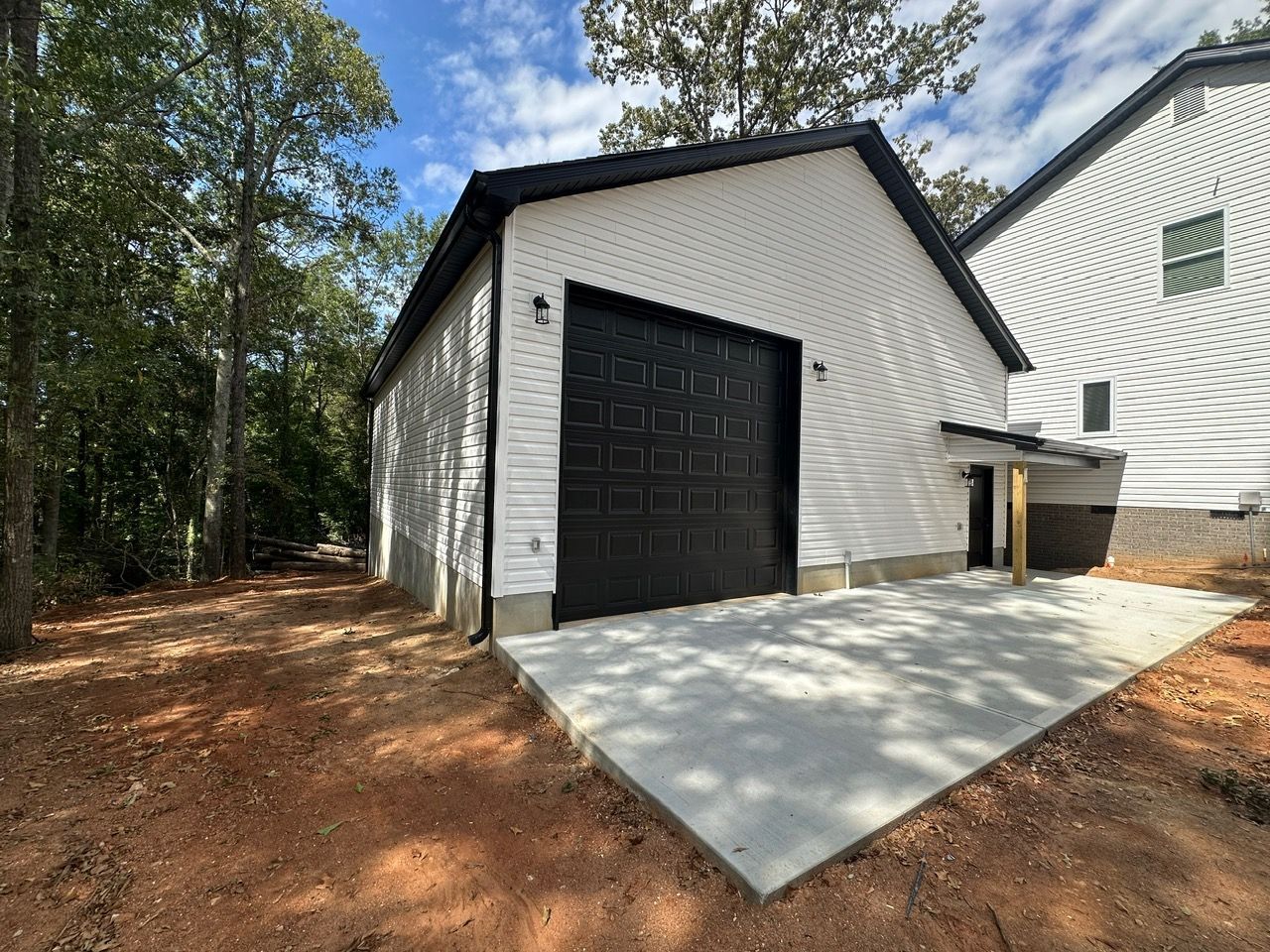 A white garage with a black door is in the backyard of a house.