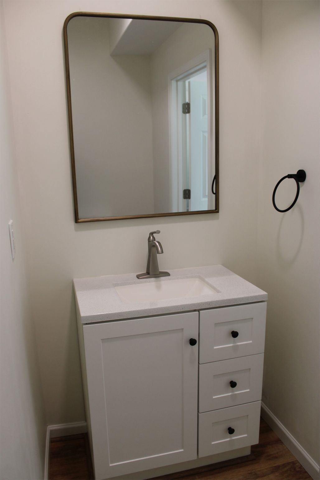 White vanity with a sink, mirror, and towel ring in a bathroom.