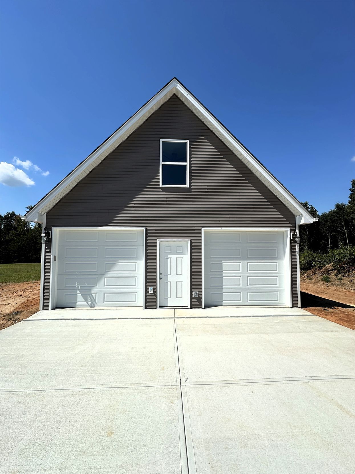 Two-car garage with gray siding, white garage doors, and a small door, set on a concrete slab under a blue sky.