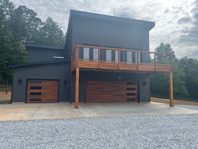 A black house with a wooden deck and garage doors.