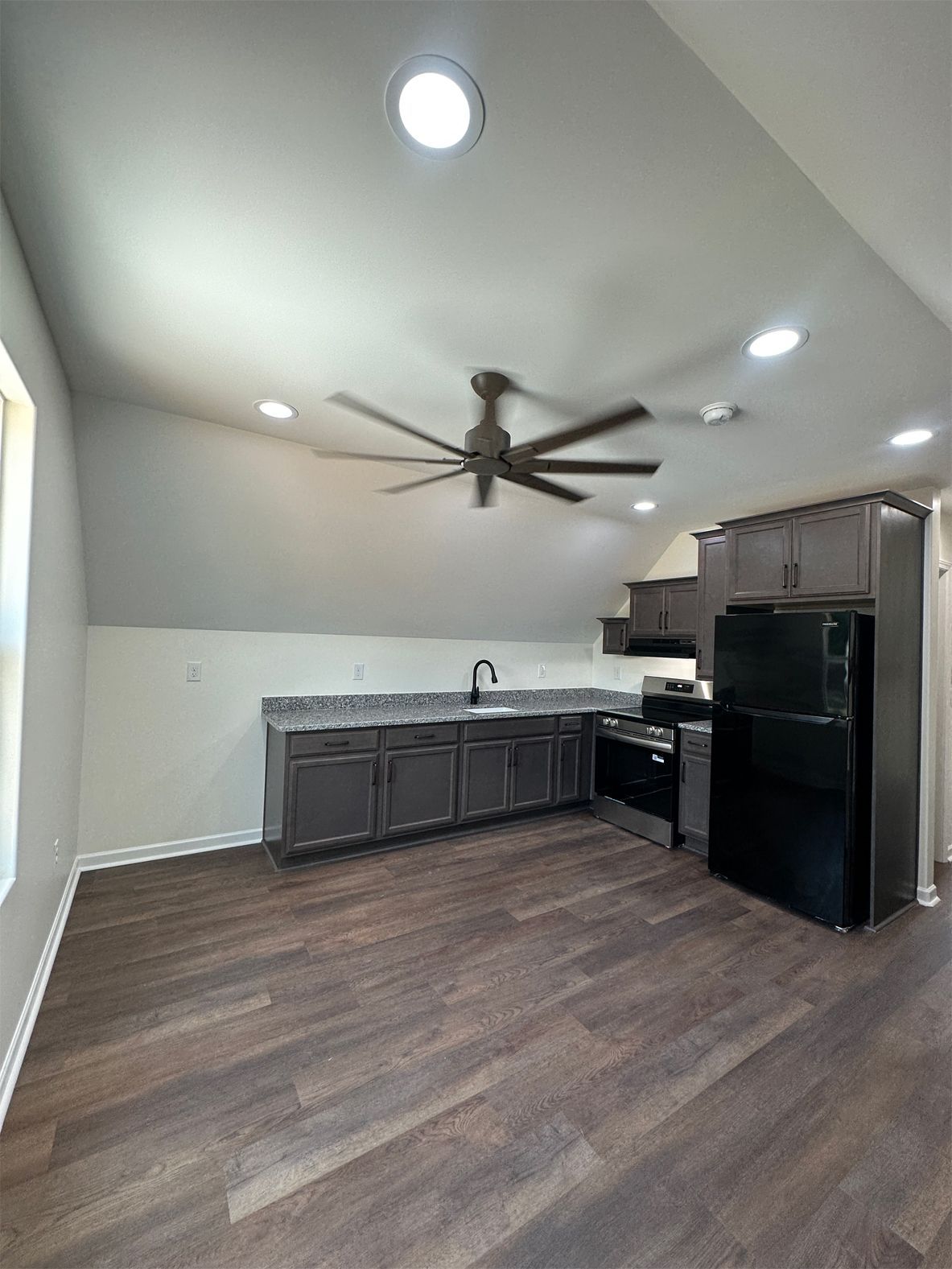 Kitchen area with dark cabinets, black appliances, and a ceiling fan. Dark wood flooring.
