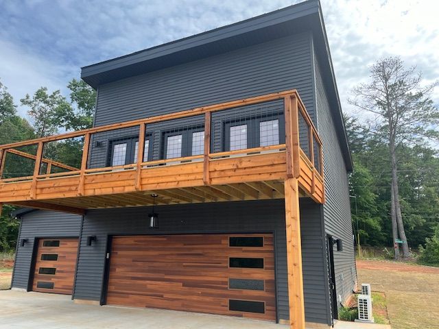 A black house with a wooden deck and a wooden garage door.