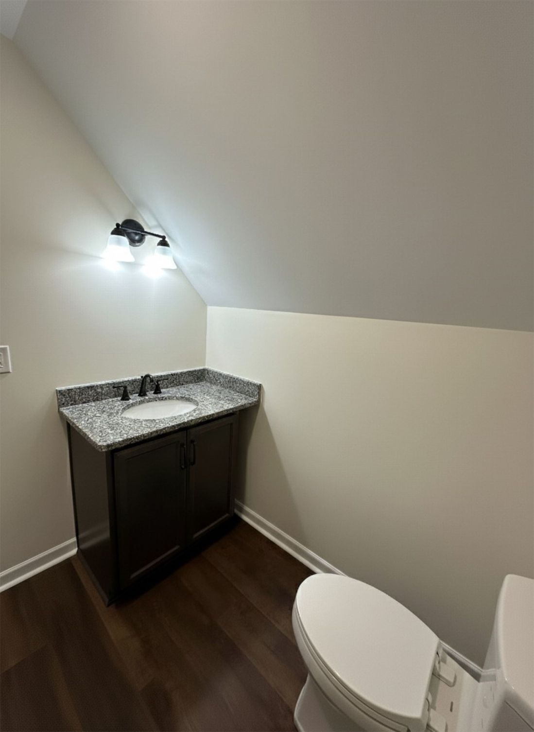Small bathroom with dark vanity, granite countertop, toilet, and sloped ceiling.