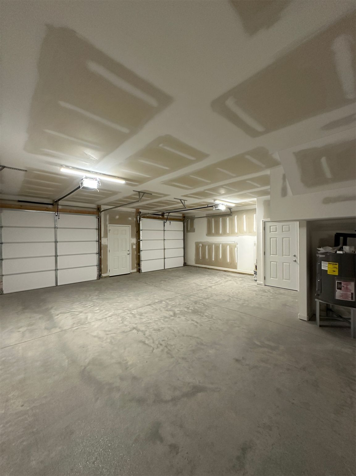Empty garage with three garage doors, a concrete floor, and unfinished walls.