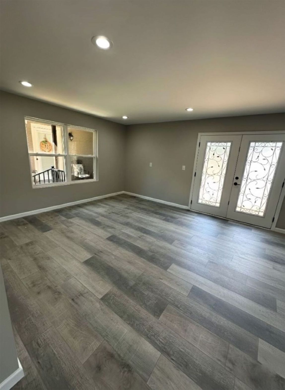 Empty room with gray wood-look floor, light gray walls, white French doors, and a window.