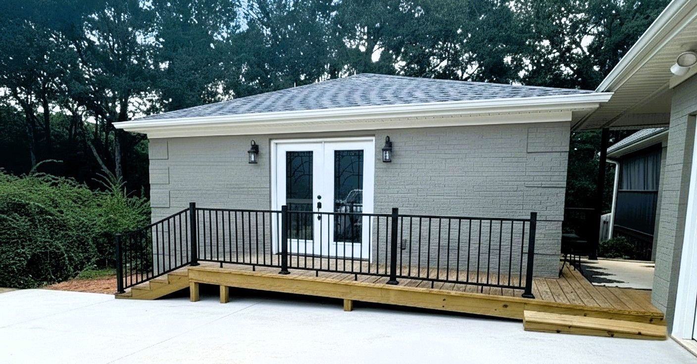 Small gray building with a wooden ramp and black railing. White double doors, two sconces, gray roof.