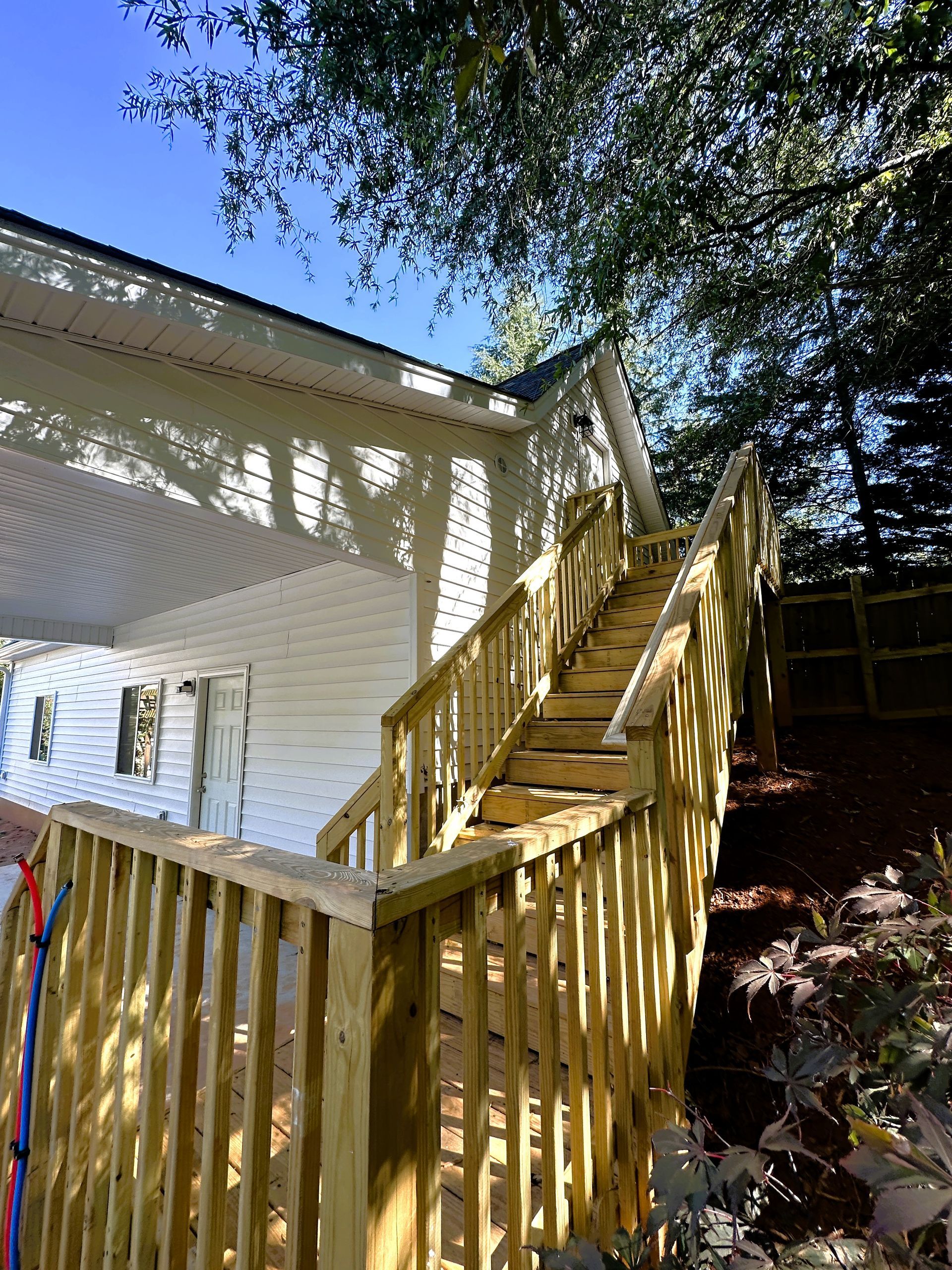 Wooden outdoor stairs leading up to a white house with a covered porch, set against a blue sky.