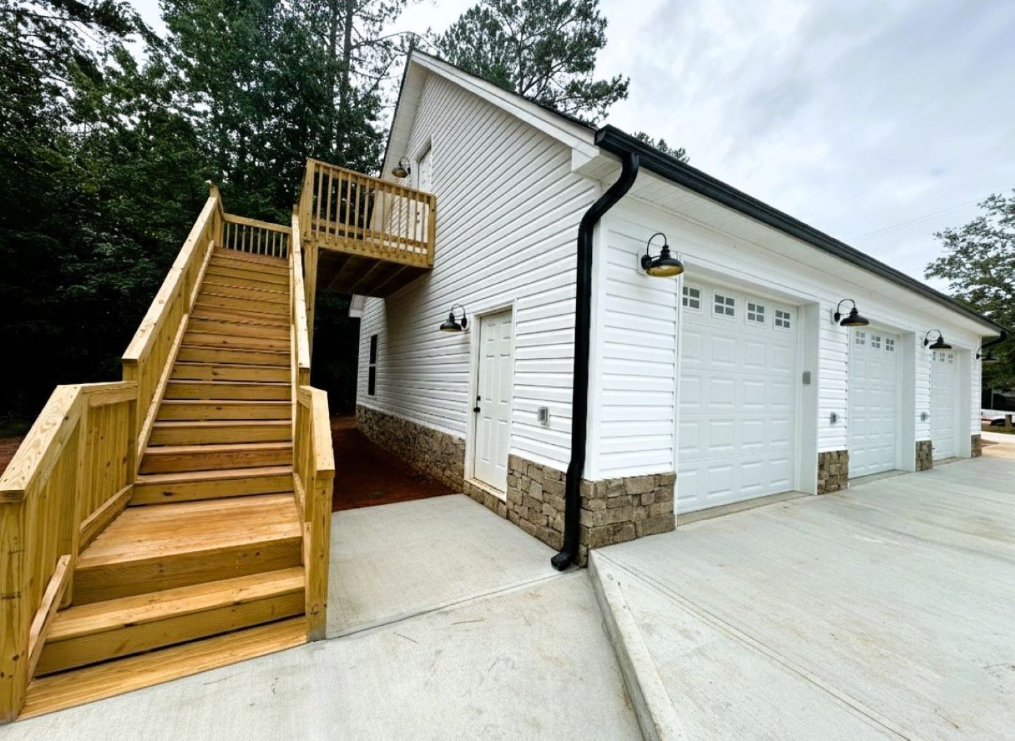 White garage with three doors, wood stairs to a deck, and brick accents.