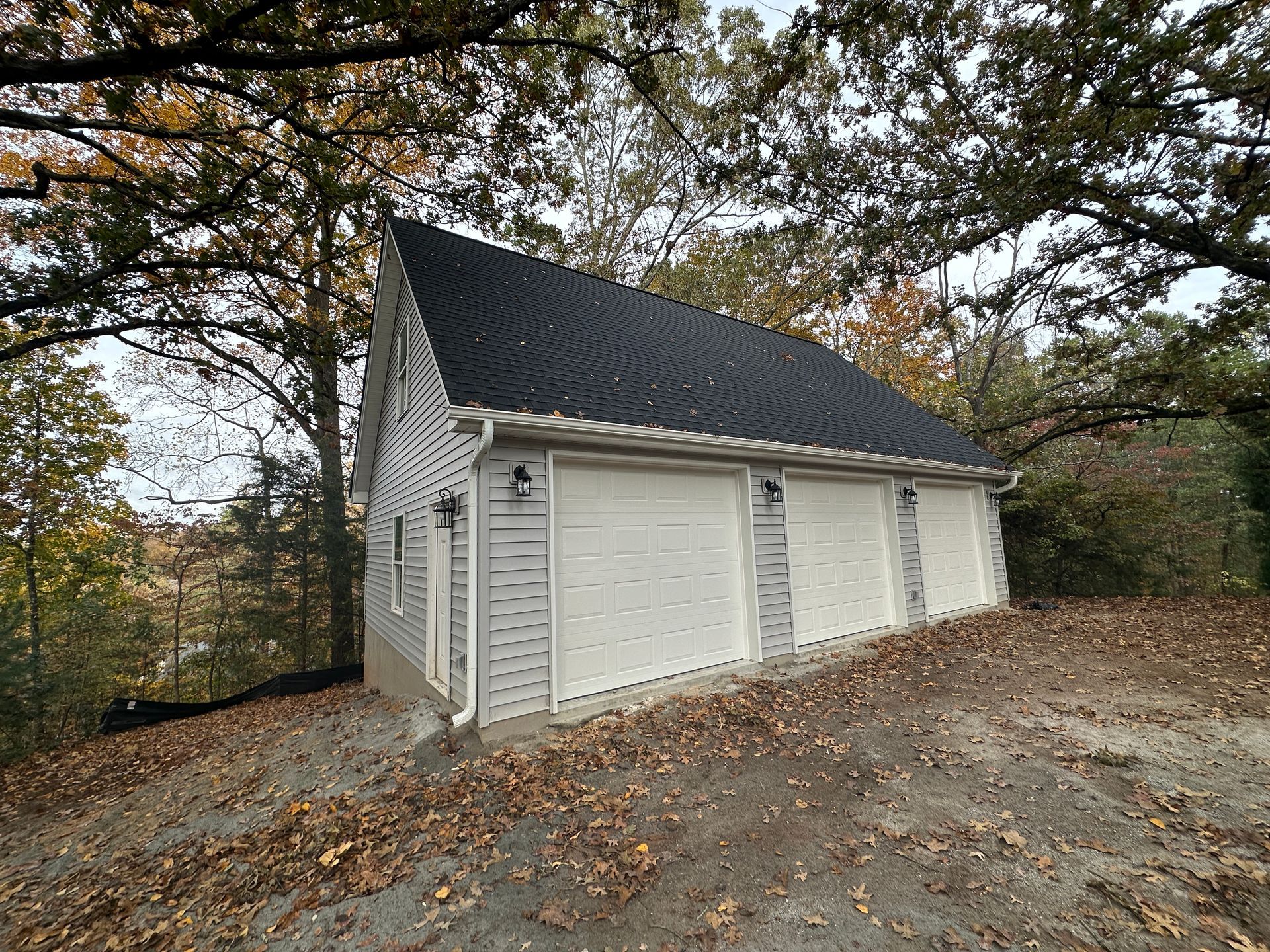 A white garage with a black roof is surrounded by trees.
