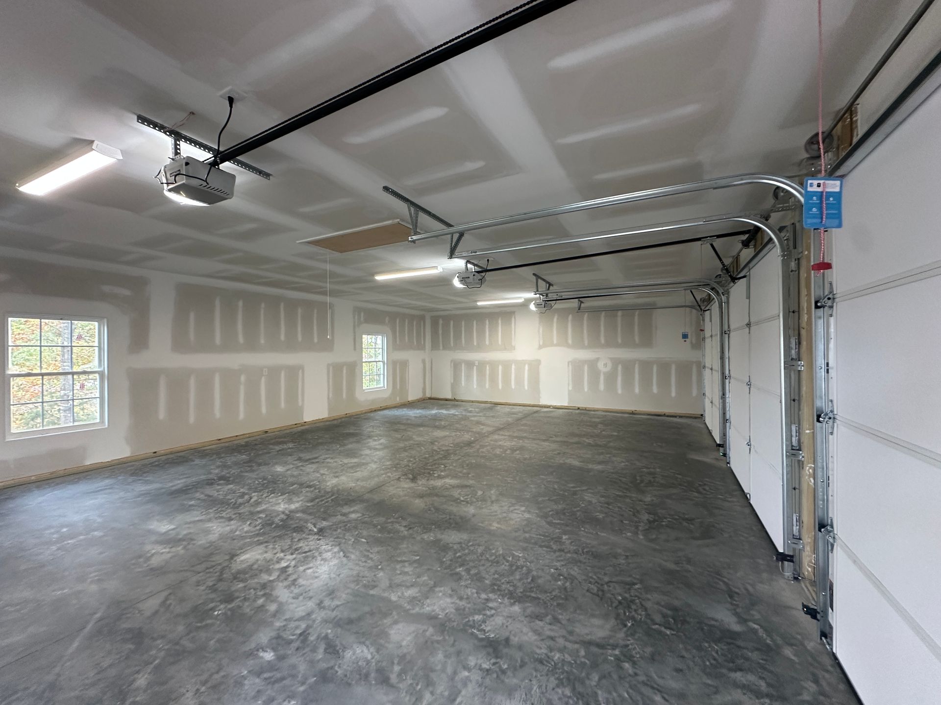 An empty garage with a concrete floor and a garage door open.