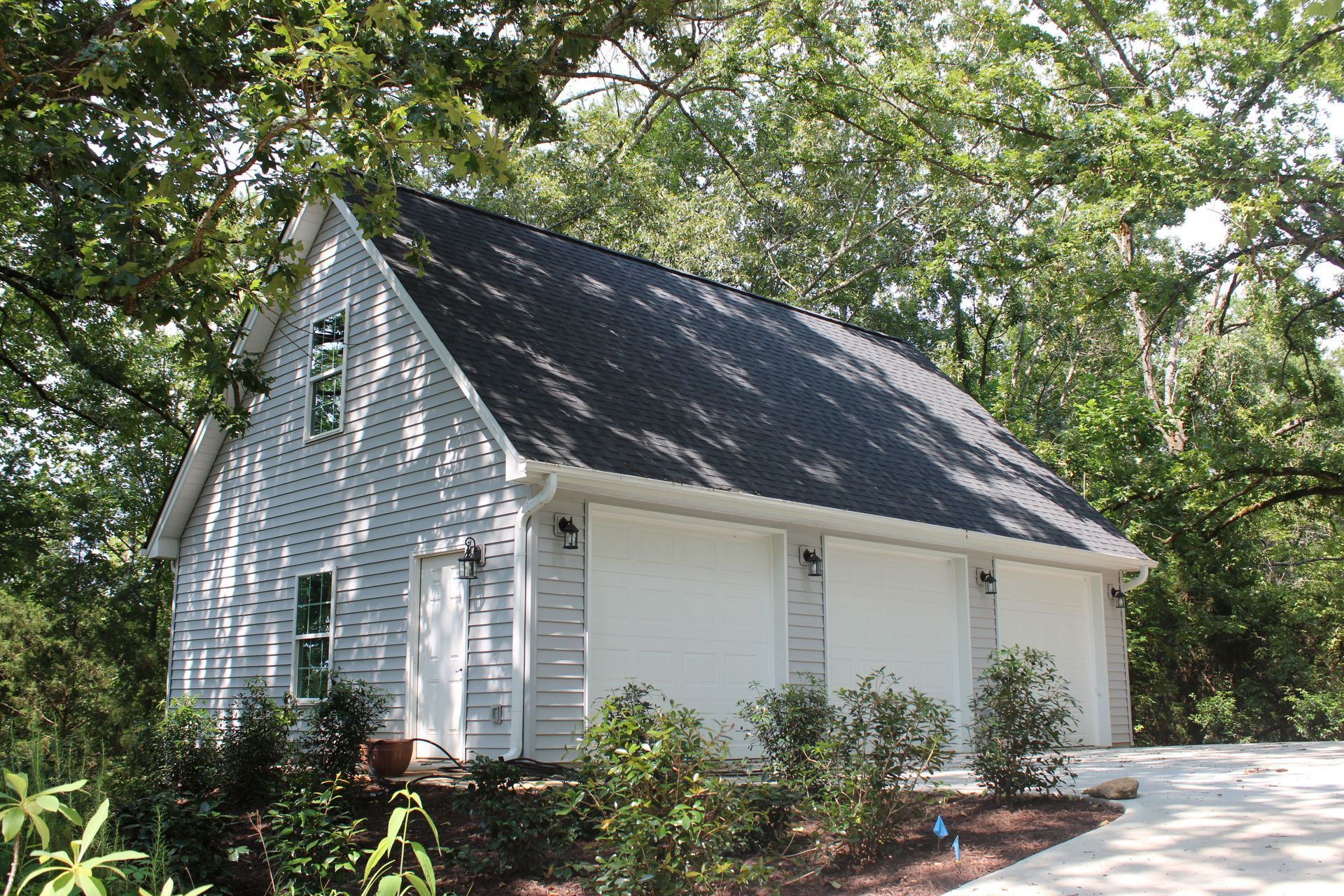 White two-story garage with three bays, surrounded by greenery and a winding driveway.