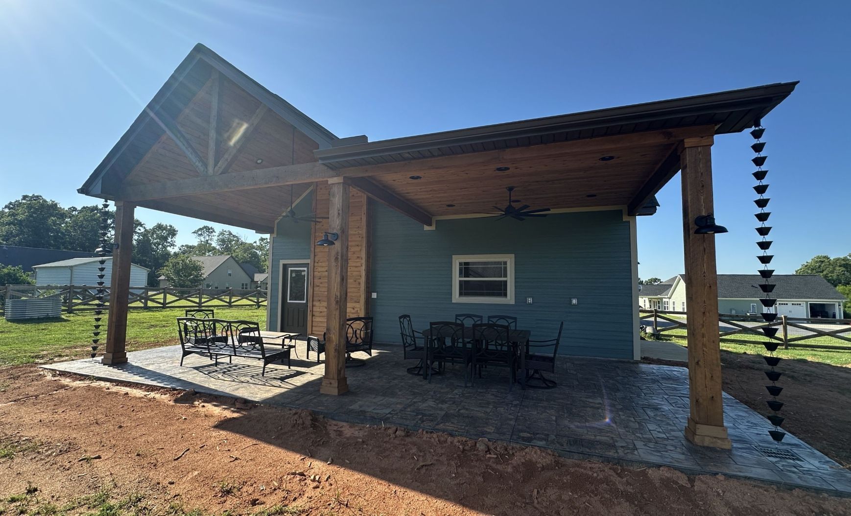 Patio with teal house, wooden posts, and a dark roof under a clear blue sky.
