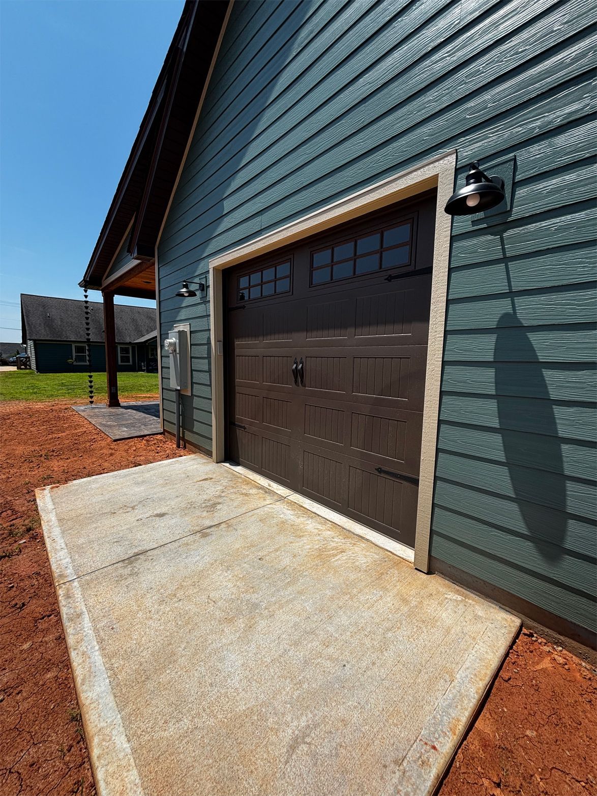 Exterior view of a teal-sided garage with a brown door and concrete walkway.