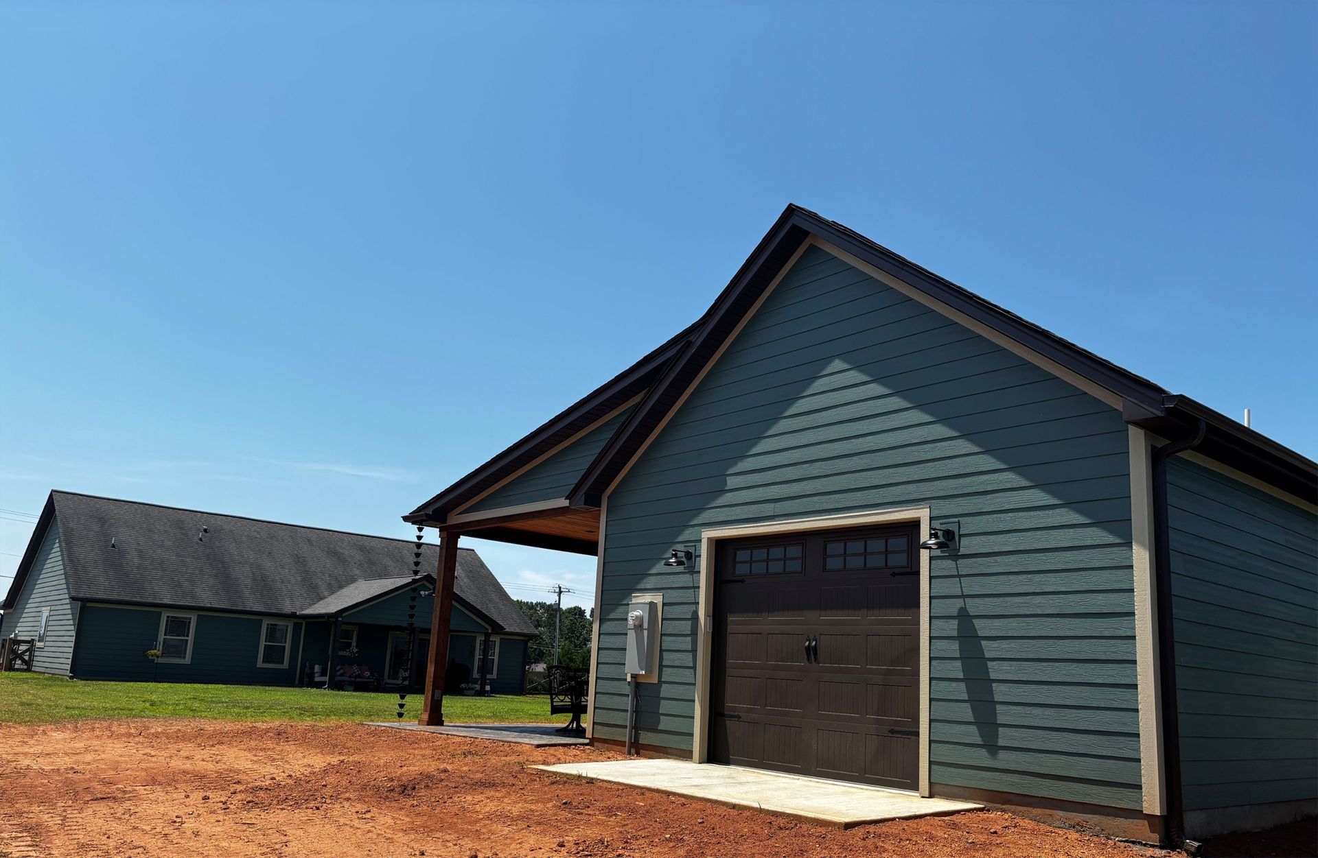 Blue building with black garage door; other building in background, blue sky.