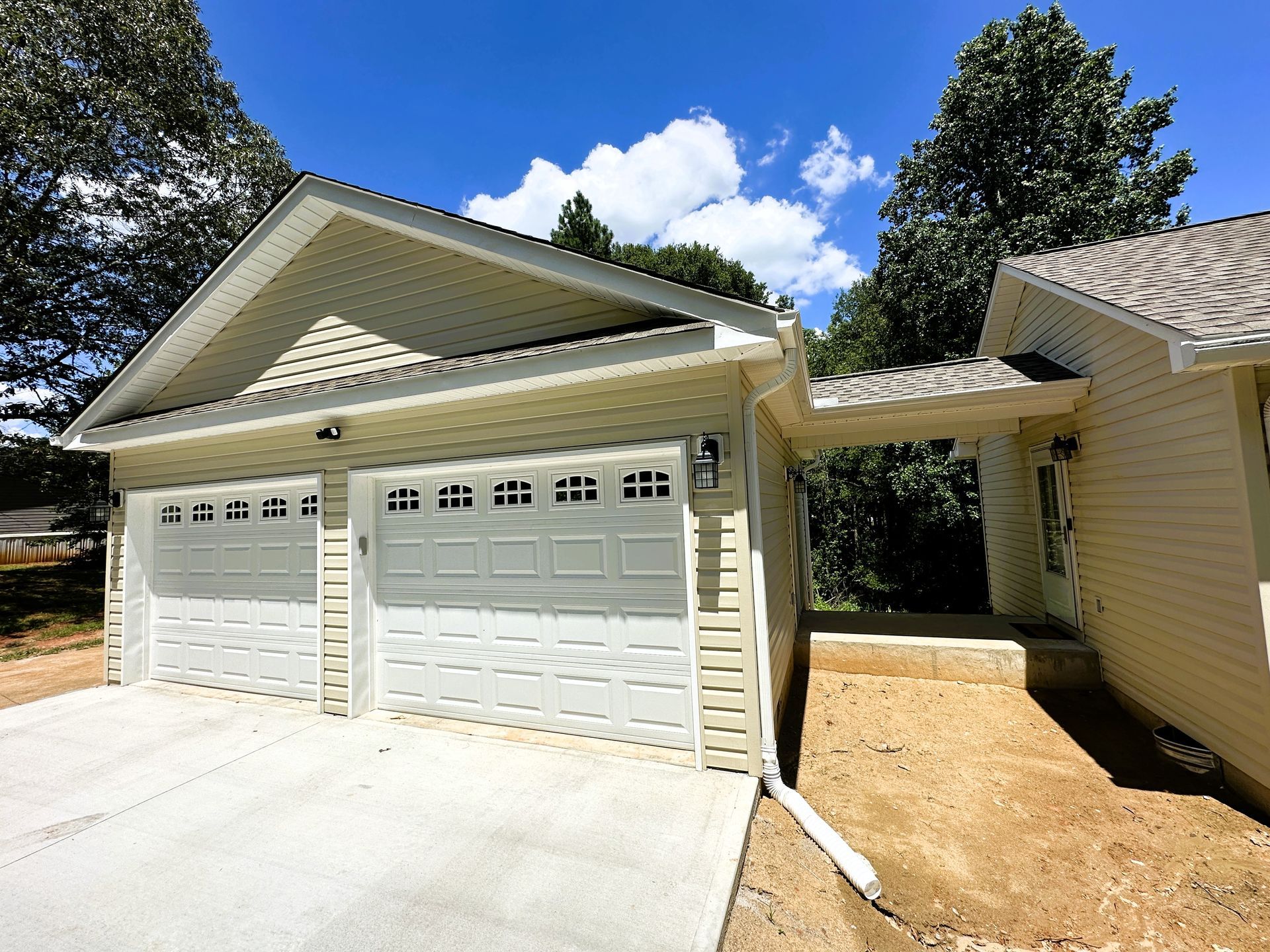 Two-car garage with white doors, light siding, and a connecting walkway to the house, under a blue sky.