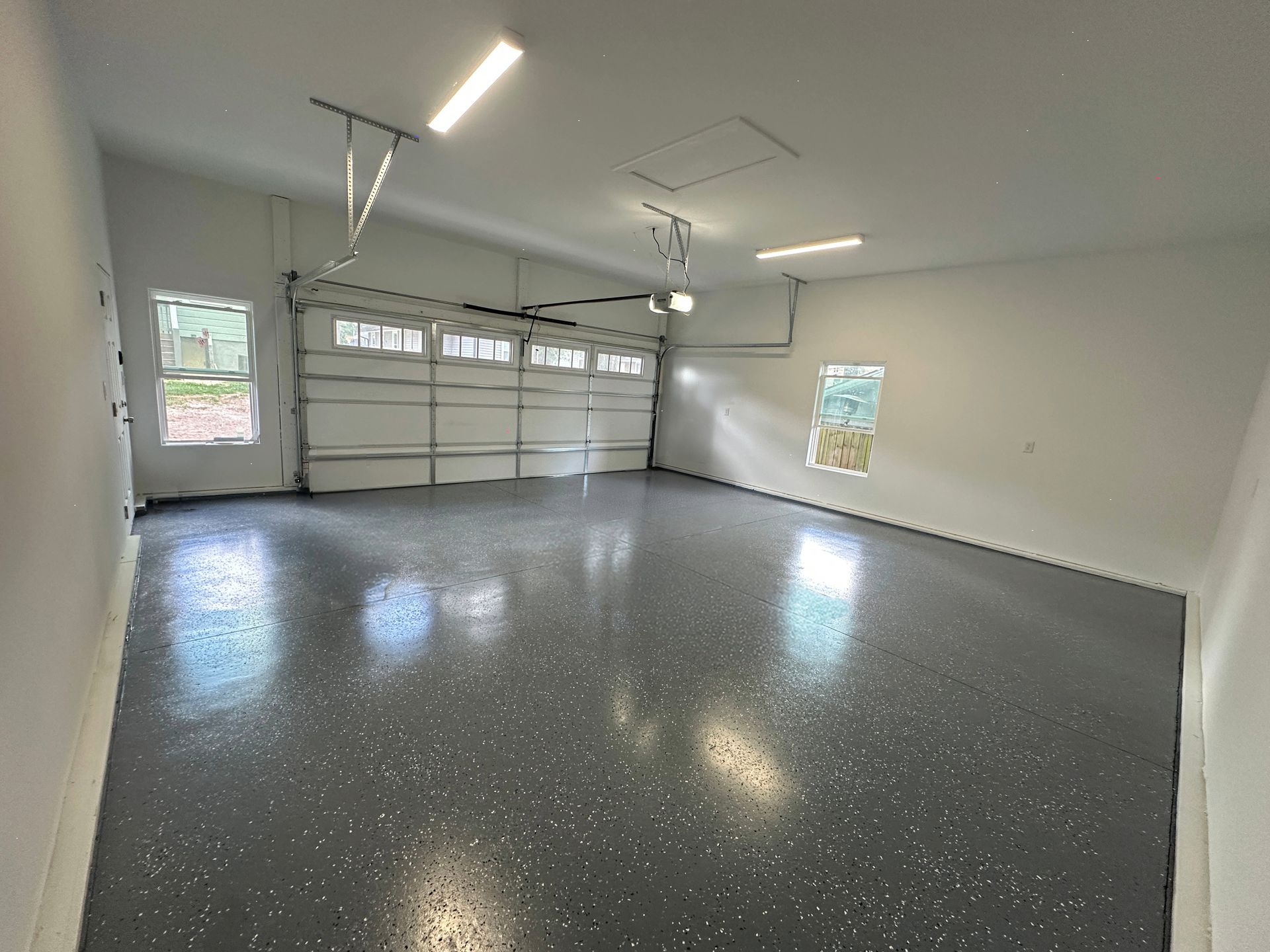 Empty garage with gray speckled epoxy floor and closed white garage door.