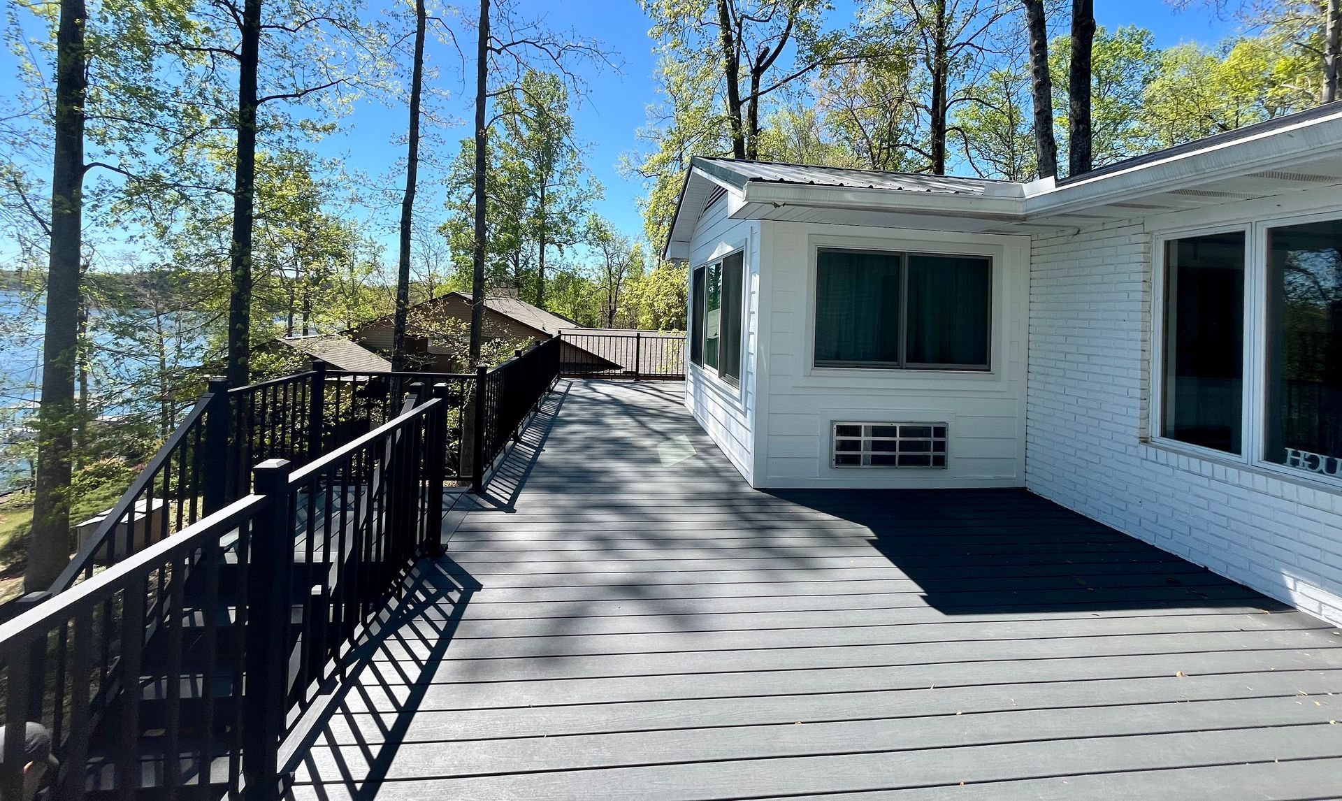 A white house with a large deck overlooking a lake surrounded by trees.
