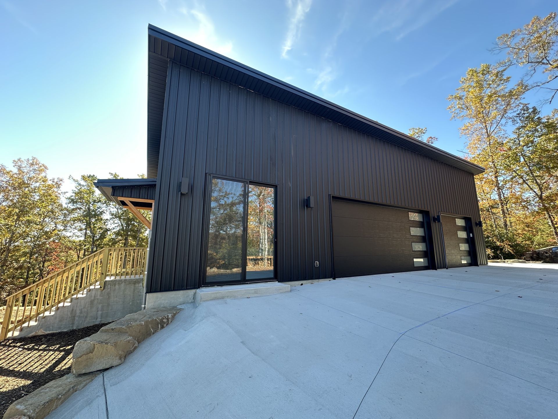 Black modern building with angled roof, glass door, and garage doors, on a sunny day.
