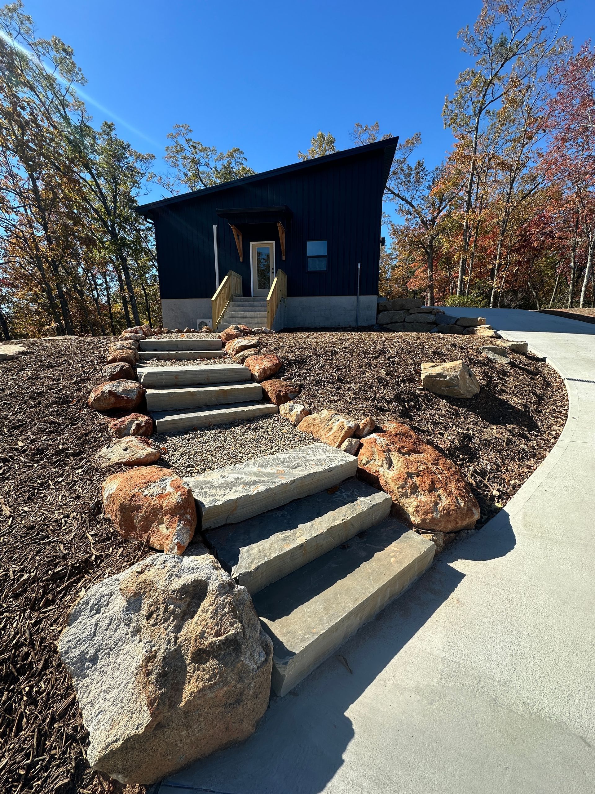 A modern cabin with a dark exterior, approached by concrete steps with large rocks.