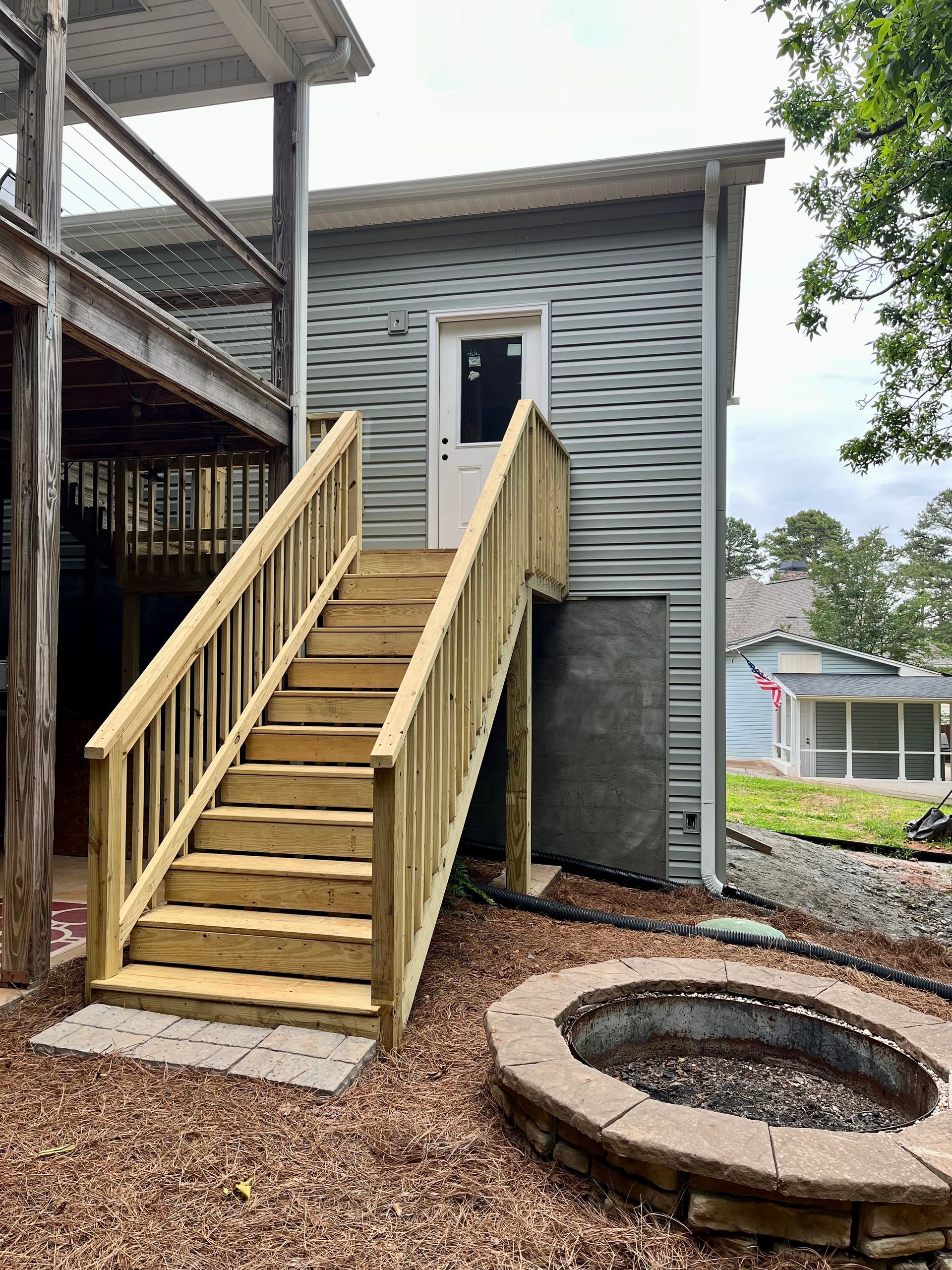 A wooden deck with stairs and a fire pit in front of a house