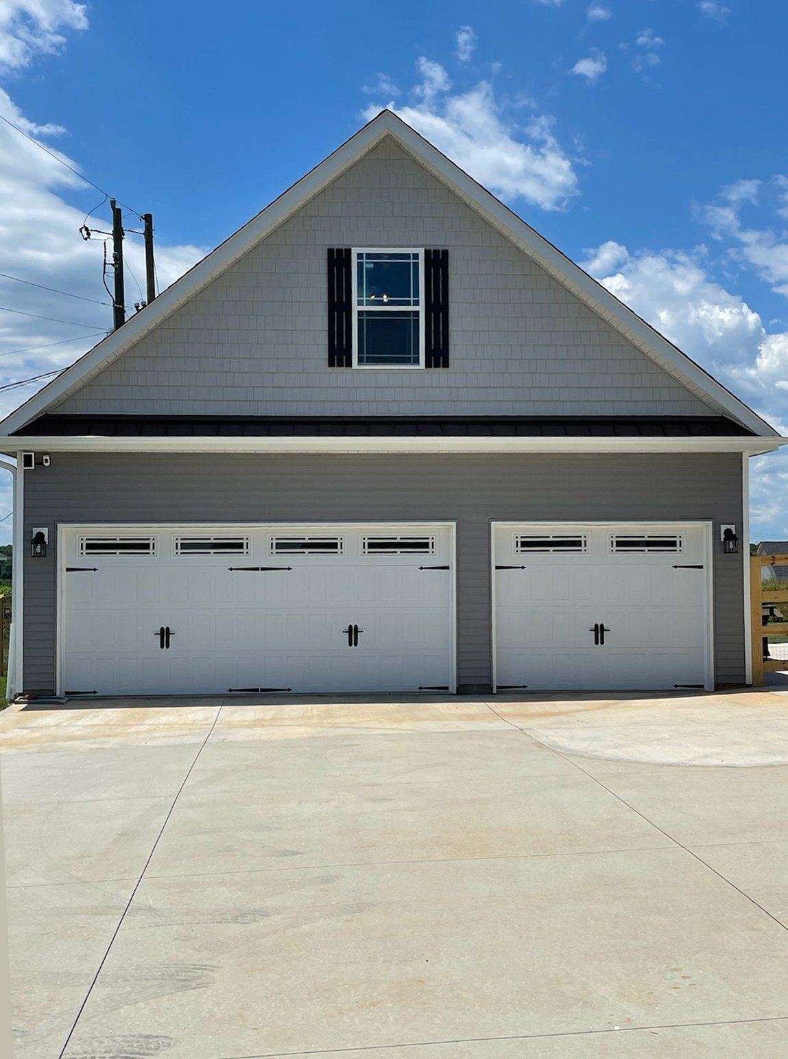 Two-car garage with white doors, gray siding, and a small window under a gable roof.