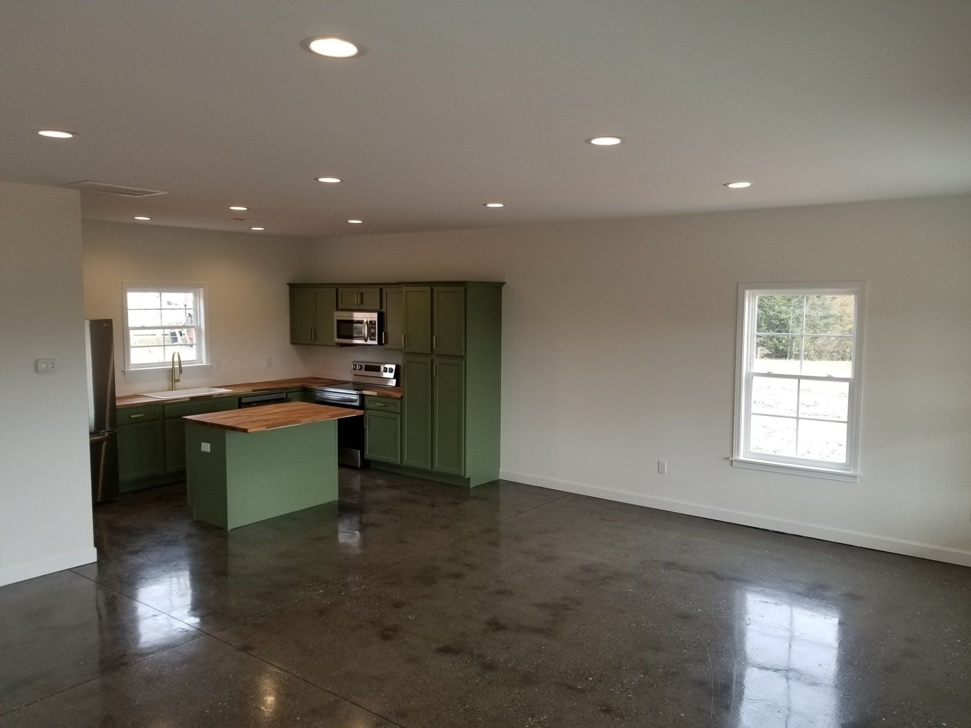 Spacious, modern kitchen with olive green cabinets, a central island, and polished concrete floor.
