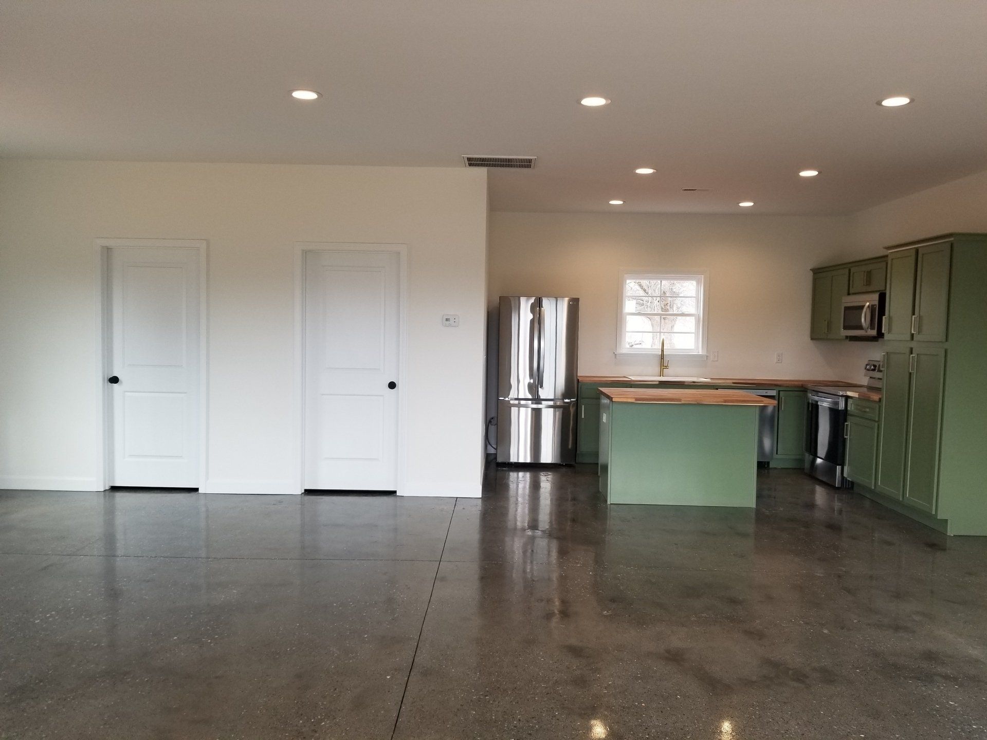 Open-concept kitchen with green cabinets and island. Stainless steel refrigerator and polished concrete floor.