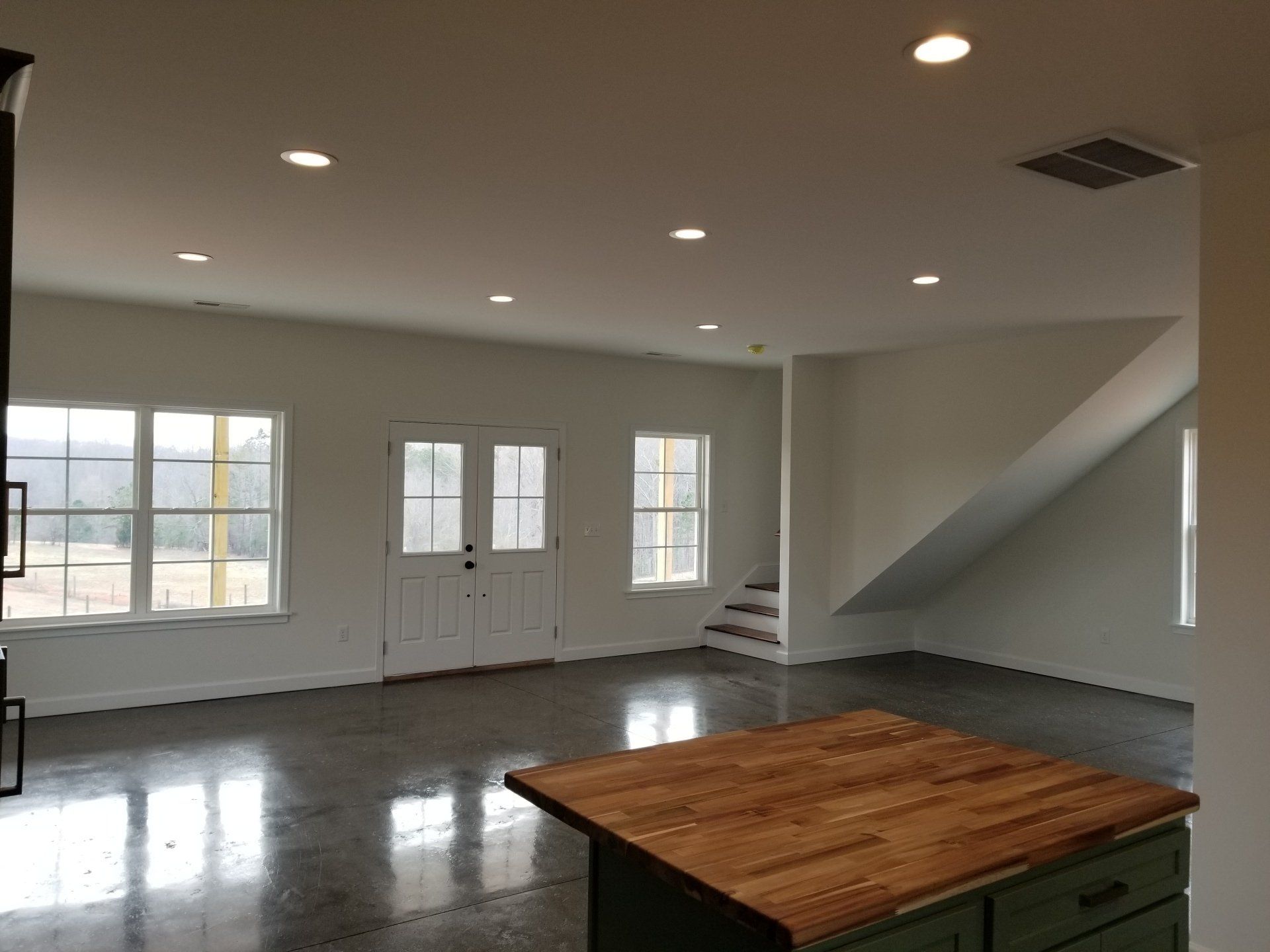 Empty interior with a concrete floor, white walls, and a wood-topped island.