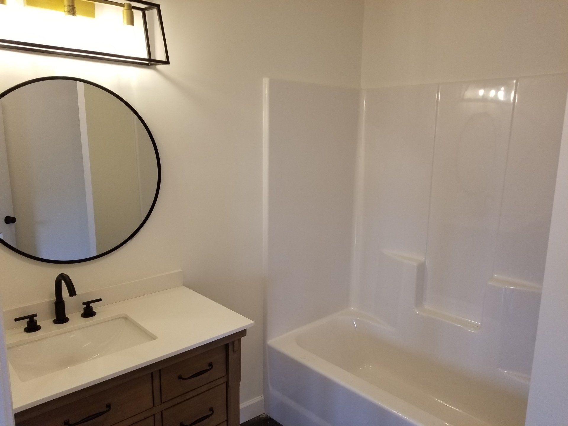 Bathroom with a vanity, round mirror, and a tub/shower combination. White and brown color scheme.