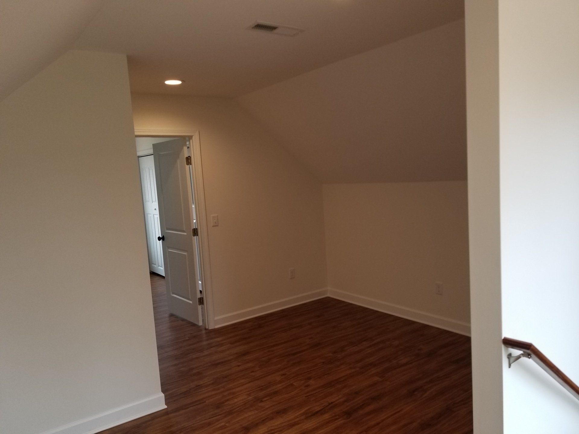 Hallway with hardwood floor, white walls, and a door at the end.