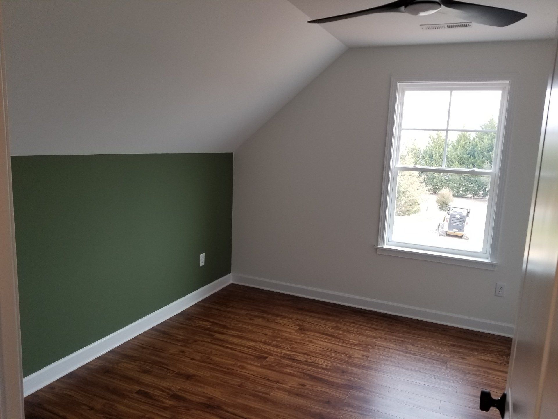 Empty bedroom with green accent wall, white walls, window, hardwood floor, and ceiling fan.