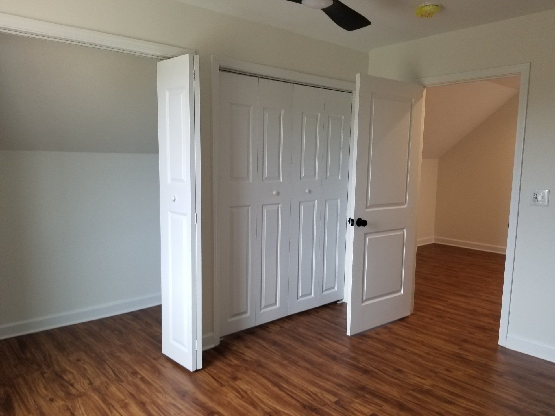 Bedroom interior with closet and doorway, white walls, wood-look floor, slanted ceiling.