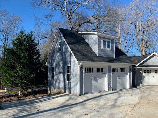 Blue and white two-story garage with three garage doors and dormer window, set on a concrete driveway.