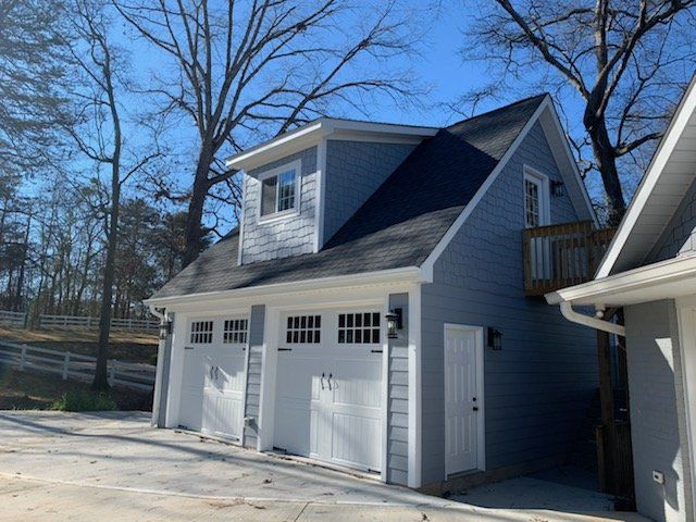 Two-car garage with light blue siding, white doors, and a dark roof, with a dormer and small balcony.